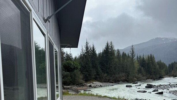 A building with large windows overlooking a river and forested mountains. - Serene Studio overlooking the river (Juneau)