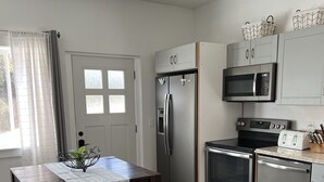 A modern kitchen with a central island, stainless steel appliances, and a dining area with a wooden table and chairs. - Serene Studio overlooking the river (Juneau)