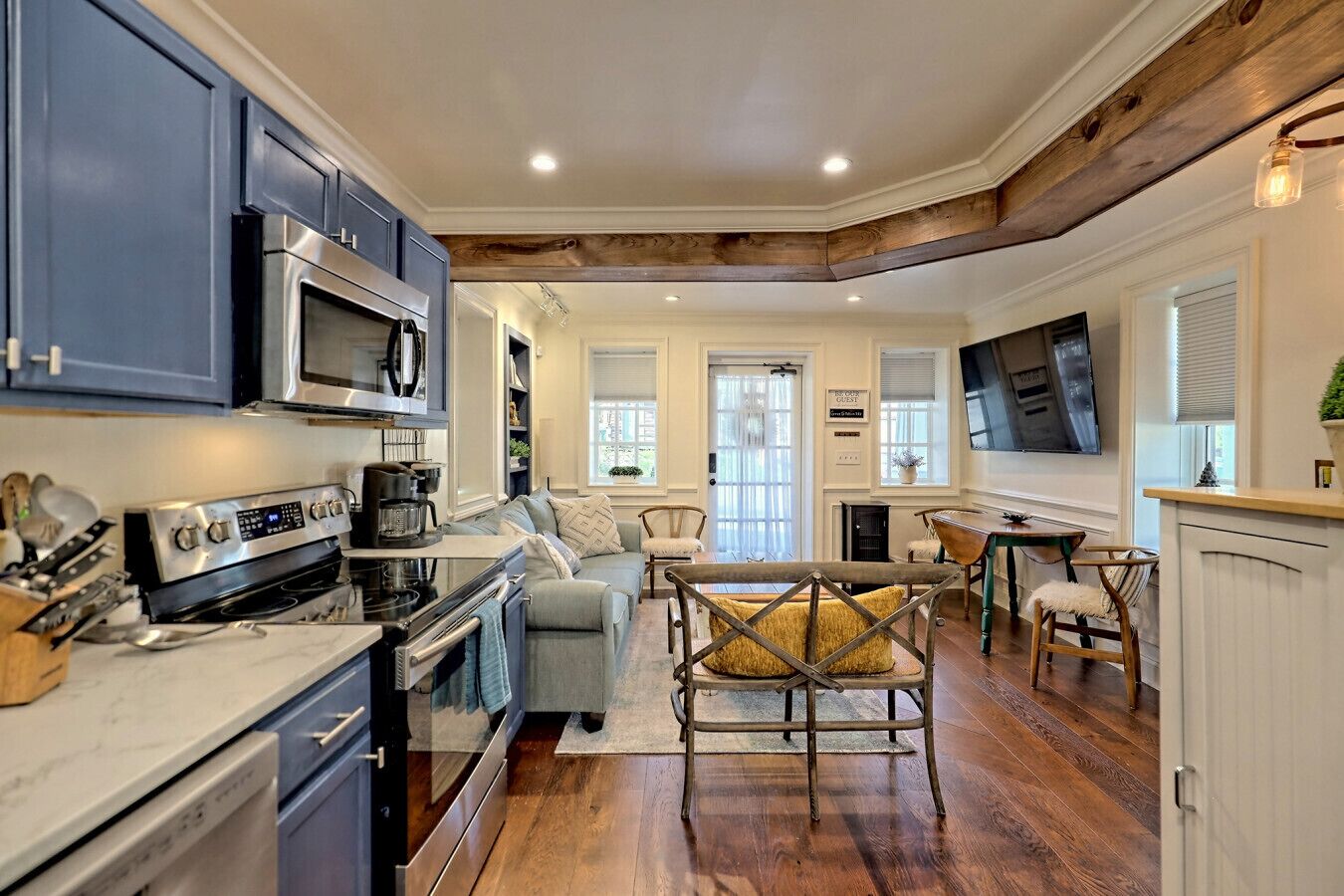A modern kitchen with stainless steel appliances, a dining area with a wooden table and chairs, and a cozy seating area with a sofa and cushions.