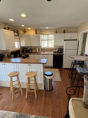 A kitchen with white cabinets, a stainless steel sink, wooden stools, and a trash can. - Cheerful historic Townsend Park bungalow in the heart of downtown!
(Montrose)