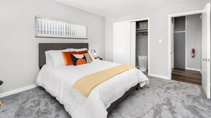 A bedroom with a bed, a nightstand, a wall-mounted light, a closet, and a door leading to another room. - Downtown Wyandotte, Clean and Cozy! (Wyandotte)