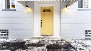 A white building with a yellow door, two windows with light fixtures, and a small porch area. - Downtown Wyandotte, Clean and Cozy! (Wyandotte)