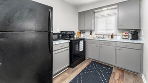 A modern kitchen with grey cabinets, a black refrigerator, a stove, and a sink. - Downtown Wyandotte, Clean and Cozy! (Wyandotte)