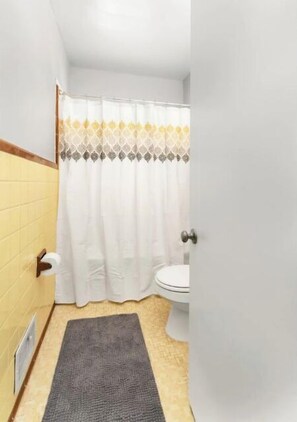 A bathroom with a toilet, a shower curtain, and a rug.