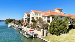 Un hôtel situé au bord de l’eau, doté de nombreux balcons, d’un quai avec des bateaux et offrant une vue sur un ciel bleu azur.
