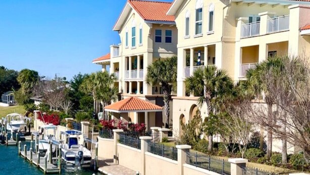 Un hôtel situé au bord de l’eau, doté de nombreux balcons, d’un port de plaisance avec des bateaux et d’un aménagement paysager luxuriant.