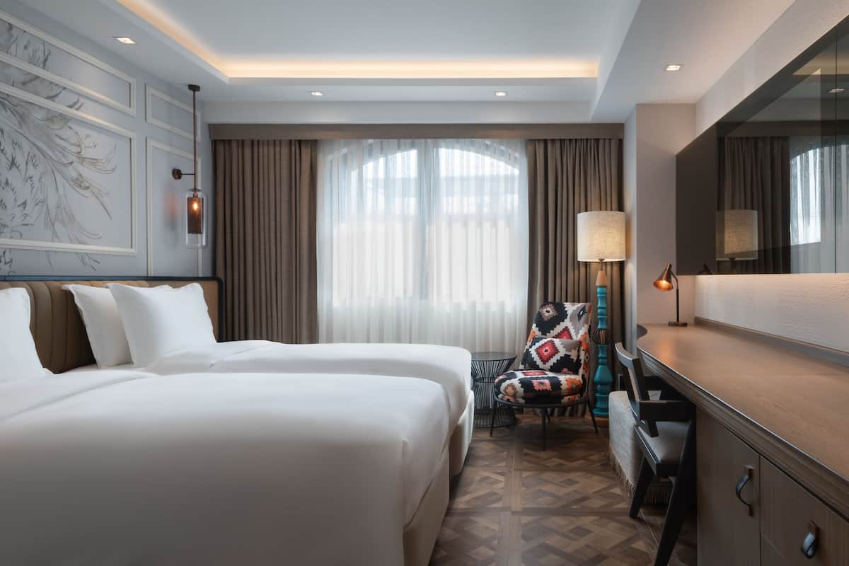 A hotel room with a large bed, a desk, a chair, a lamp, and a large mirror.