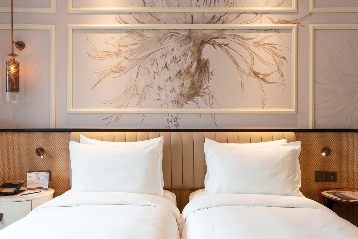 A hotel room with a large framed artwork above the bed, a modern headboard, and a bedside table with a lamp.