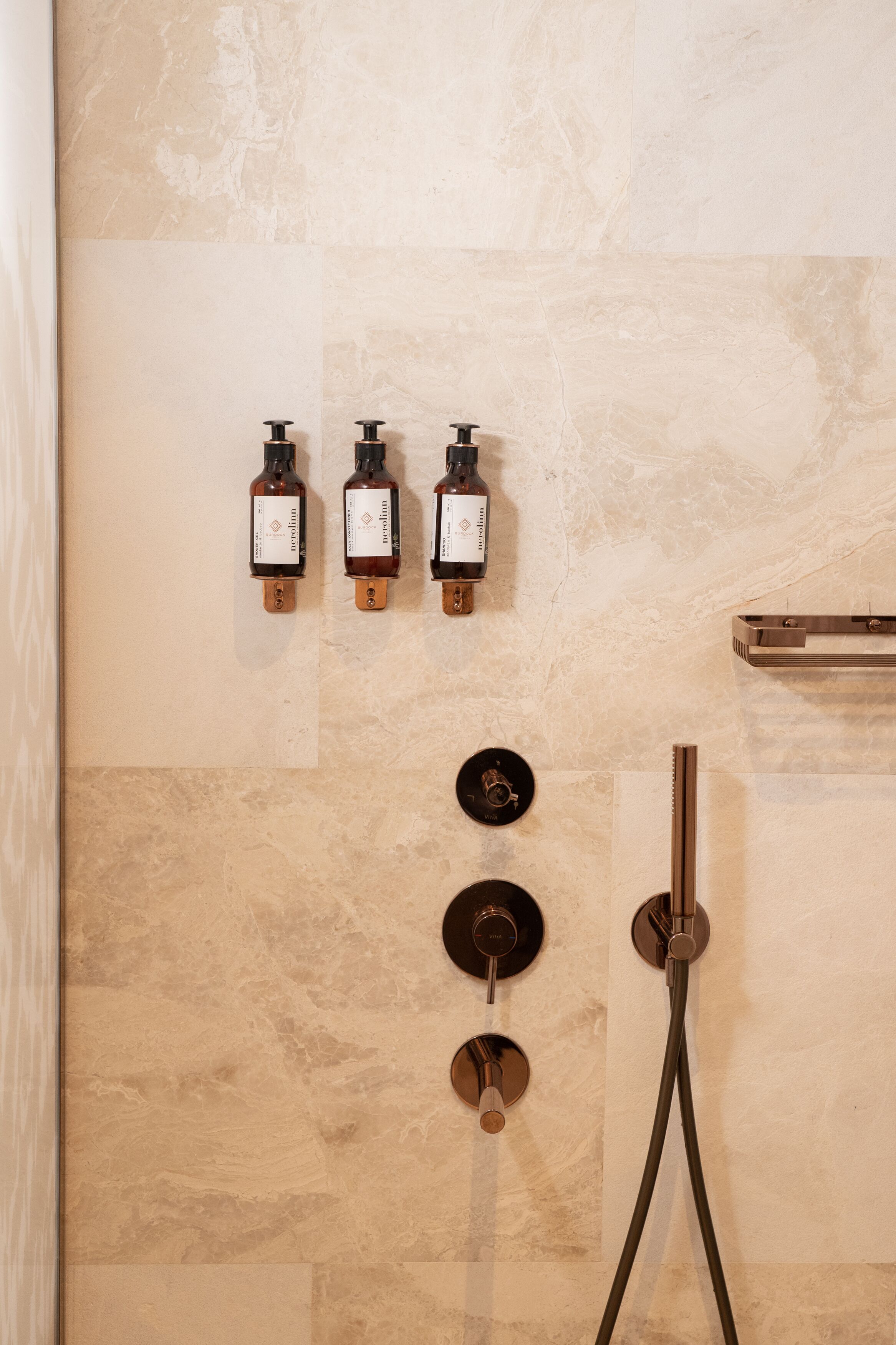 A bathroom with three wall-mounted soap dispensers, a showerhead, and a towel rack.