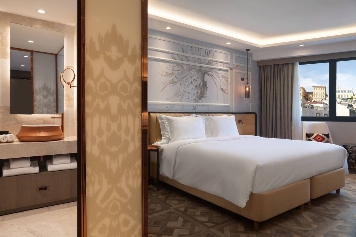 Hotelkamer met een groot bed, een badkamer met spiegel en wastafel, en uitzicht op de stad.