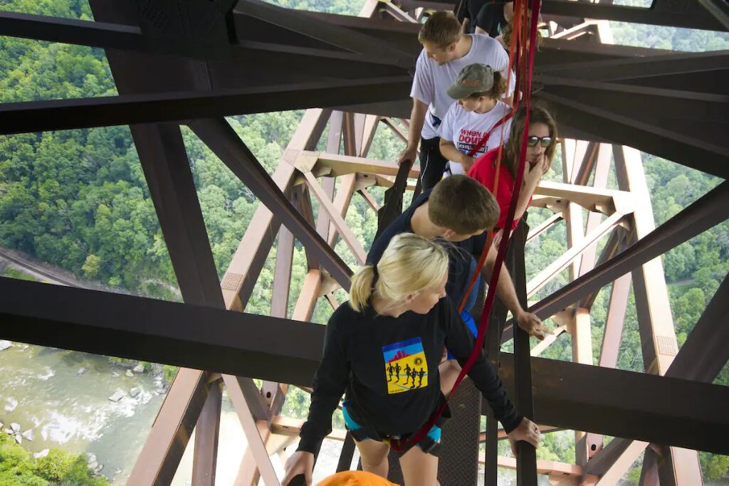 Een groep mensen op een hoge brug, met uitzicht op een rivier en bos daaronder.