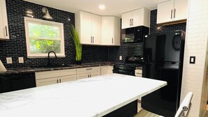 A modern kitchen with a large island, black and white cabinetry, and a black refrigerator. - Tuxedo Touch Modern 2BR Townhouse (Smyrna)