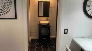 A bathroom with a white sink, a black cabinet, and a mirror above it. The floor has black and white hexagonal tiles. - Tuxedo Touch Modern 2BR Townhouse (Smyrna)