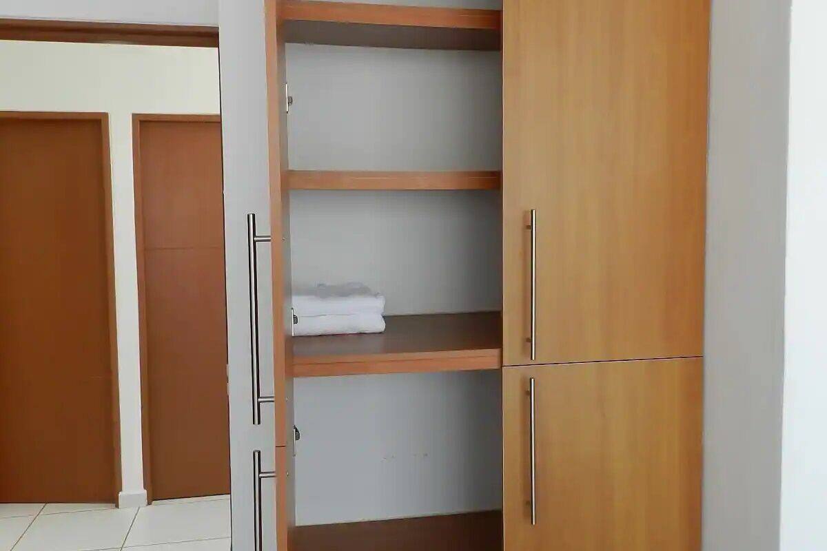 A wooden wardrobe with multiple shelves and a hanging rod, located in a room with tiled flooring and wooden doors.