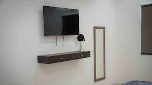 Un dormitorio con cama, televisor montado en la pared, mesita de noche con espejo y armario.