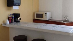 A small kitchenette with a microwave, a coffee maker, and a water dispenser. There are two stools in front of the counter.