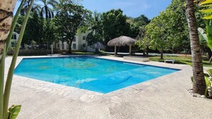 A swimming pool with a decorative pattern in the center, surrounded by palm trees and a thatched-roof structure.