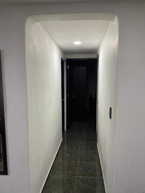 A narrow, well-lit hallway with white walls and dark tiled flooring.