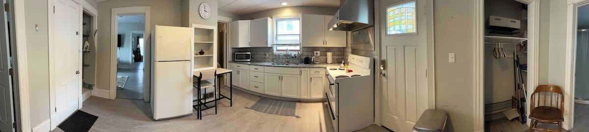 Una cocina moderna con armarios blancos, un refrigerador y un microondas. Hay una zona de comedor con mesa y sillas.