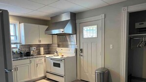 Una cocina compacta con armarios blancos, una campana extractora de acero inoxidable, un horno empotrado y un cubo de basura.