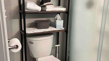 A bathroom with a white toilet, a black shelf unit with towels, a basket, and a toilet paper holder.