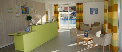 A reception area with a green counter, several framed certificates, a potted plant, and a pool view through a glass door.