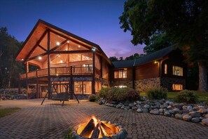 A wooden lodge with a covered porch, a fire pit, and a stone exterior.