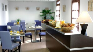 Un comedor de hotel con sillas azules, una larga barra con cestas de comida y una lámpara.
