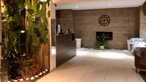 A reception area with a wooden reception desk, a wall-mounted clock, and a large potted plant. - Escapade de Ski à Valberg av/Vues des Montagnes! (Guillaumes)