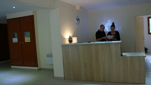 Una reception in un atrio di hotel, con un orologio a parete, una porta a sinistra e un piccolo oggetto decorativo sulla scrivania.