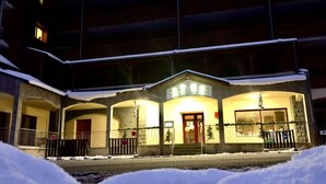 Un hotel con area esterna coperta, diversi balconi e terreno innevato.