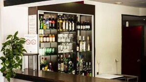A bar area with a variety of liquor bottles, framed posters on the wall, and a potted plant.