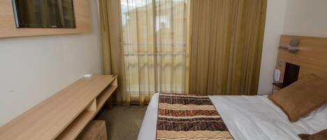 A hotel room with a bed, a desk, a chair, and a window with curtains.