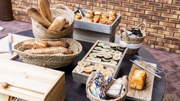 A variety of breads and pastries displayed in baskets and wooden boxes, suggesting a bakery or food service area.