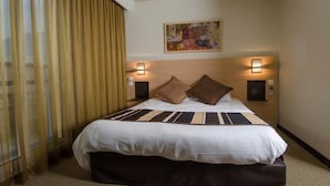 A hotel room with a large bed, two wall-mounted lamps, and a painting above the bed.
