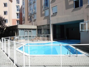 A swimming pool with a white safety fence, surrounded by a building with multiple windows and balconies. - 5mn de la Gare | Chambre Double Confort + Parking (Gap)