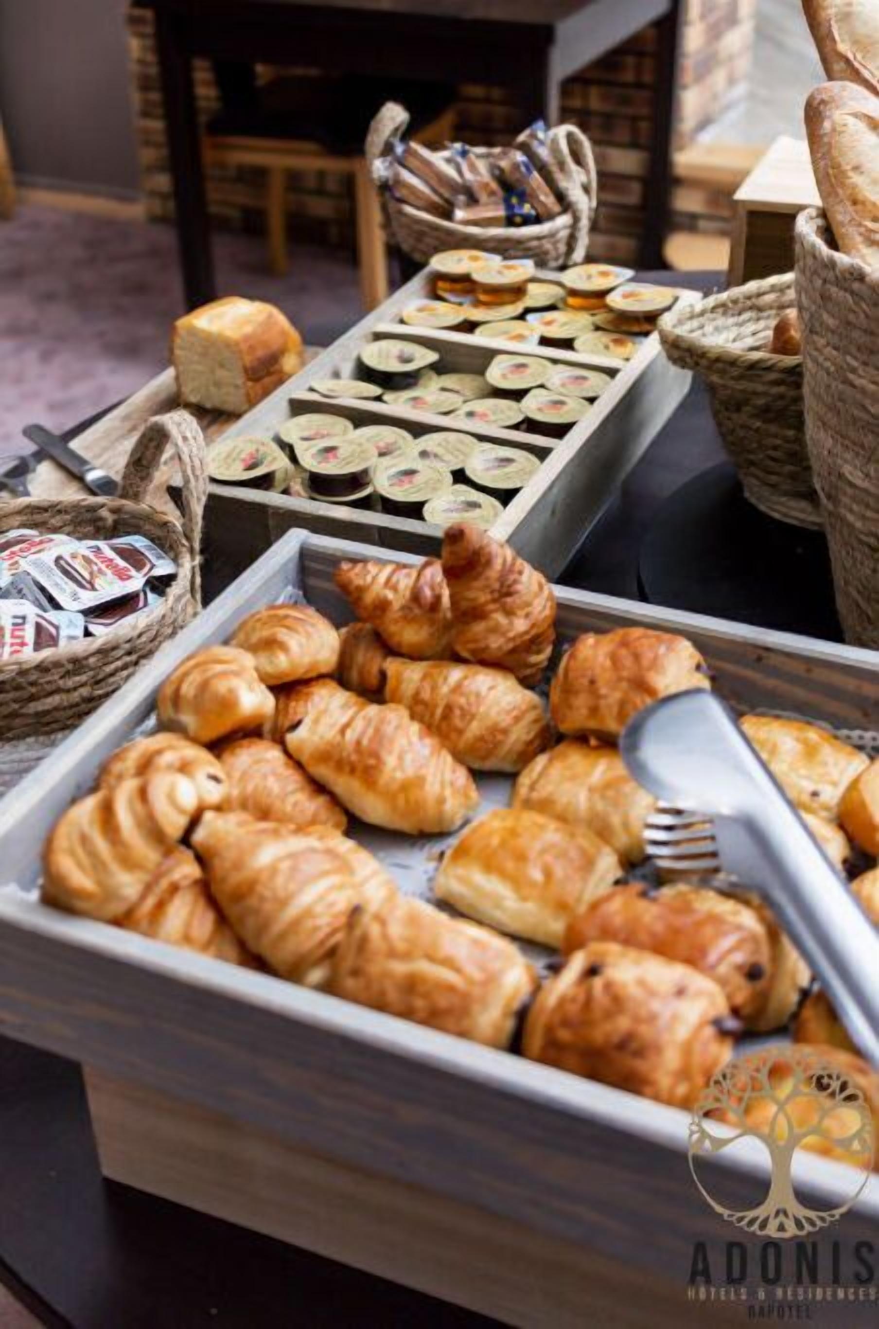 A buffet with various pastries and bread, including croissants and muffins, arranged on trays.