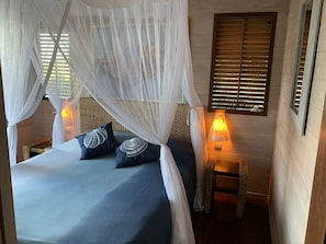 A bed with a canopy, two bedside lamps, and a small wooden stool.