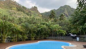 En pool omgivet af en træterrasse og frodig vegetation, med et bjerglignende landskab i baggrunden.