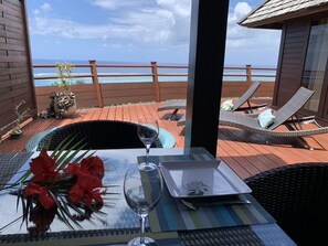 A dining area with a table set for two, a potted plant, and a view of the ocean.