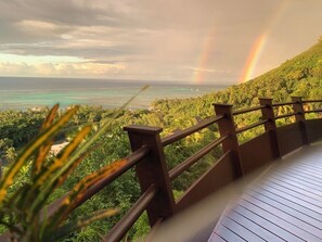 Eine Holzterrasse mit Blick auf eine tropische Landschaft und einem Regenbogen.