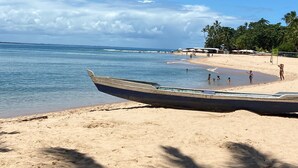 A beach with a boat, palm trees, and people. - Pousada Apoema (Maraú)