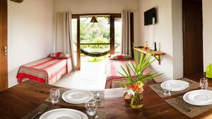 A room with a dining table set for two, a hammock, and a view of a lush garden. - Pousada Apoema (Maraú)
