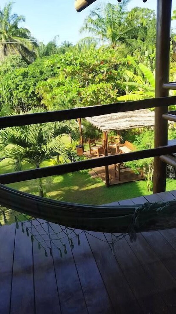 Un hamac sur une terrasse en bois donnant sur un jardin luxuriant, avec une table et des chaises en bois.