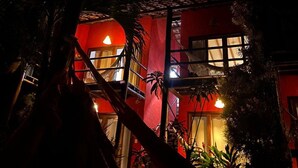 A building with a red facade and a balcony, under a night sky with a visible moon. - Pousada Apoema (Maraú)