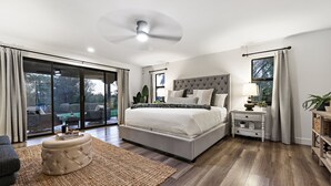 A bedroom with a large bed, a ceiling fan, a nightstand, and a view through the window.