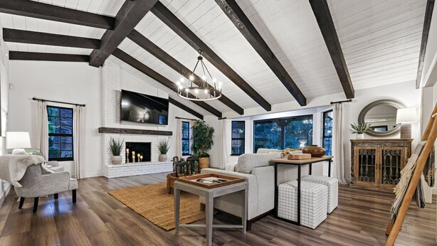 A spacious living room with a fireplace, wooden beams, and large windows.