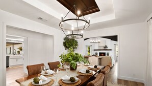 A dining area with a long wooden table, wicker chairs, and a chandelier.
