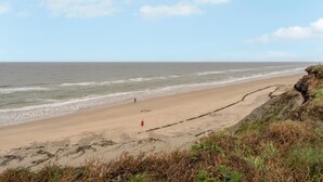 A beach with a clear sky, waves, and a person walking.