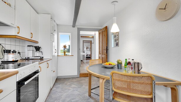 A modern kitchen with white cabinets, a stove, and a dining area with a round table and wicker chairs.
